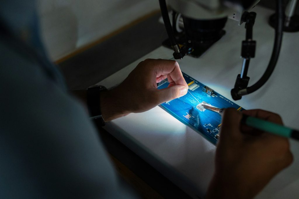 Technician soldering a circuit board under microscope.